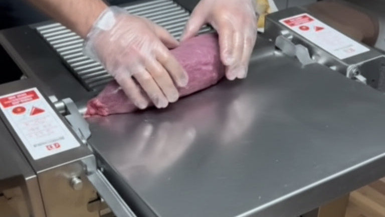 Person using a meat grinder with a bowl below on a wooden floor.